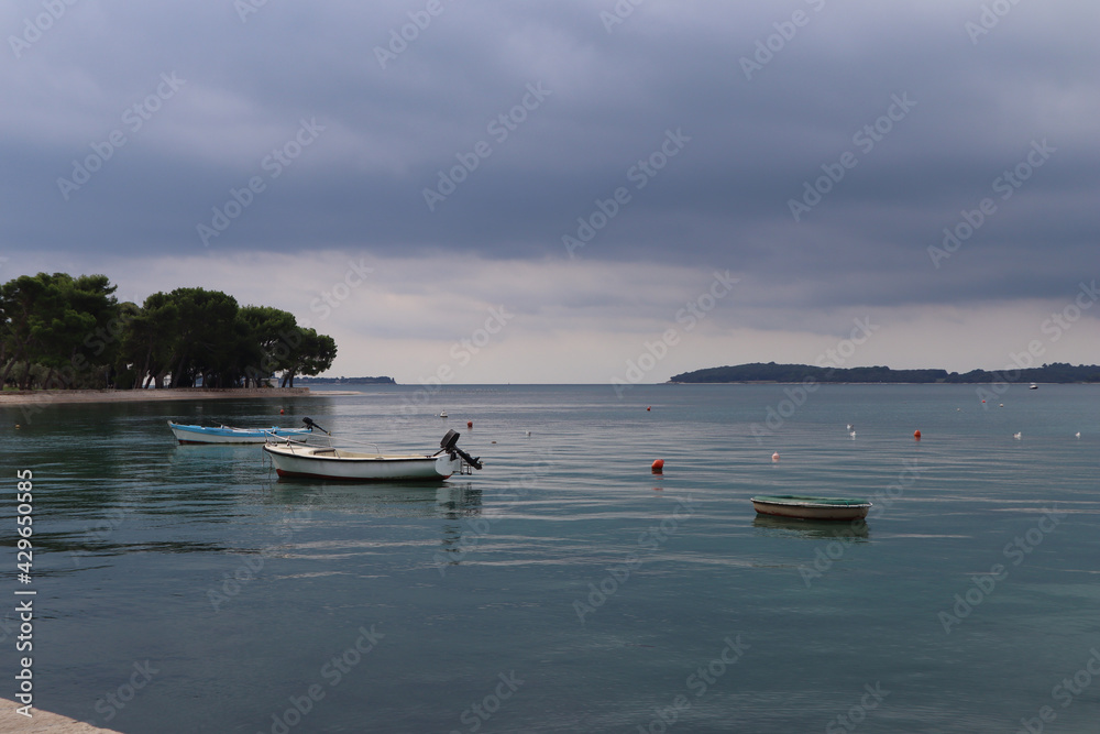 Thunderous sky and calm sea with boats, gray clouds are reflected in calm blue water. Seascape calm at sea, boats anchored storm clouds, island Brijuni on the horizon, Croatia Thunderous sky and calm sea with boats, gray clouds are reflected in calm blue water. Seascape calm at sea, boats anchored storm clouds, island Brijuni on the horizon, Croatia