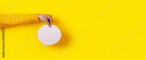 Talk bubble speech icon in hand over yellow background, panoramic layout