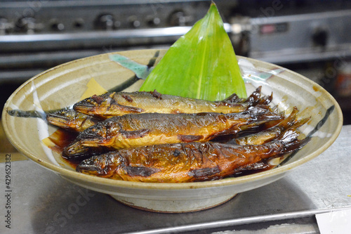 寿司屋のカウンターで、大皿に盛り付けられた丸ごと一尾の鮎の甘露煮。