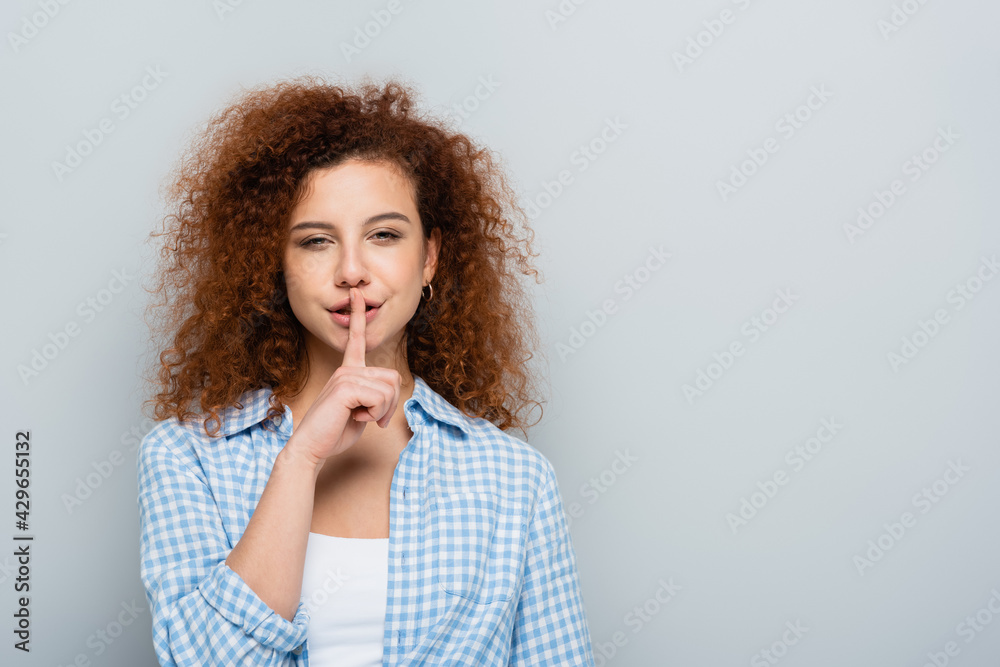 sly woman looking at camera and showing hush gesture isolated on grey sly woman looking at camera and showing hush gesture isolated on grey