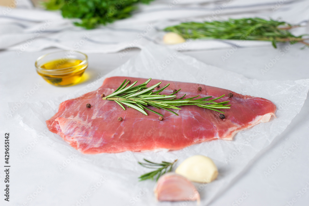 Fresh raw flank steak beef with rosemary, garlic, olive oil on light background. Classic marinades recipe for roasting or grilling. Meat food menu, copy space