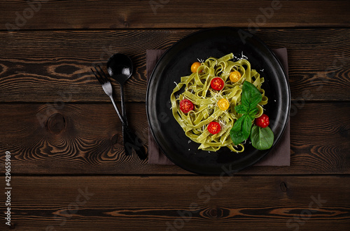 Green pasta with spinach, cherry tomatoes and cheese, on a wooden table, horizontal, no people,