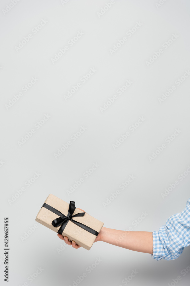 cropped view of woman holding gift box with black ribbon on grey background with copy space