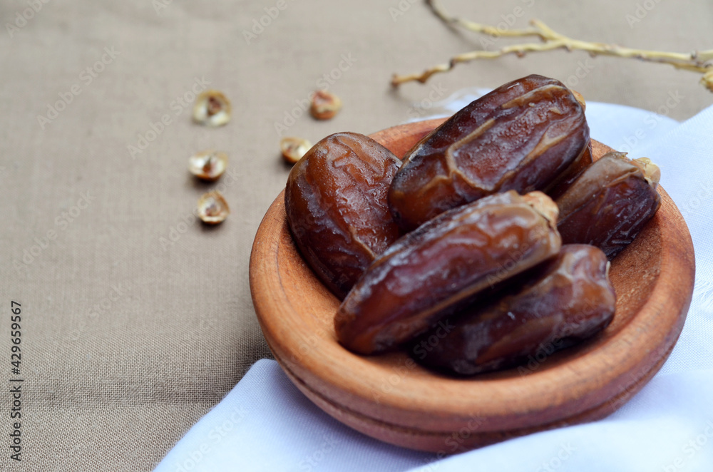 Dates (Phoenix dactylifera) on a wooden bowl on a white and brown cloth background. food for breaking the fast during Ramadan for Muslims. selective focus Dates (Phoenix dactylifera) on a wooden bowl on a white and brown cloth background. food for breaking the fast during Ramadan for Muslims. selective focus