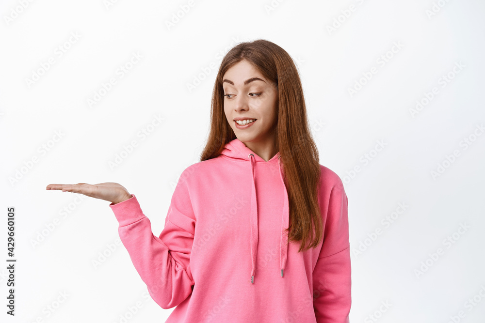 Cute teen girl student, holding copyspace on palm, display product in her hand against white background, smiling and looking at object, white background Cute teen girl student, holding copyspace on palm, display product in her hand against white background, smiling and looking at object, white background