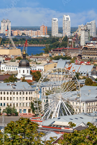 Ferris wheel and bell tower with copper roof and gilded dome in the old Podil district in Kyiv, cityscape on a summer day.