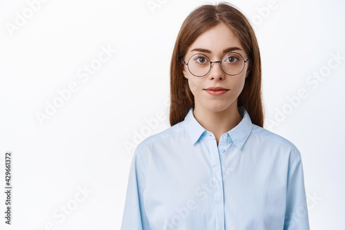 Close up of young office woman in bussiness blue shirt and glasses, looking like professional with determined face, standing over white background