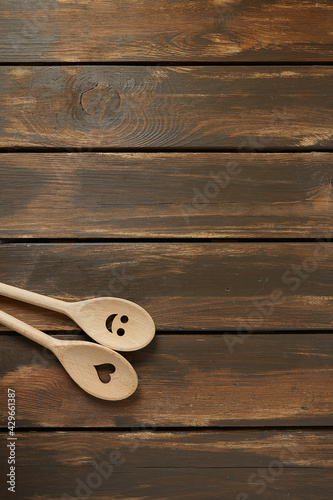 Two wooden spoons on brown wooden surface. Cooking concept. Spoons are with a smile and heart on it.