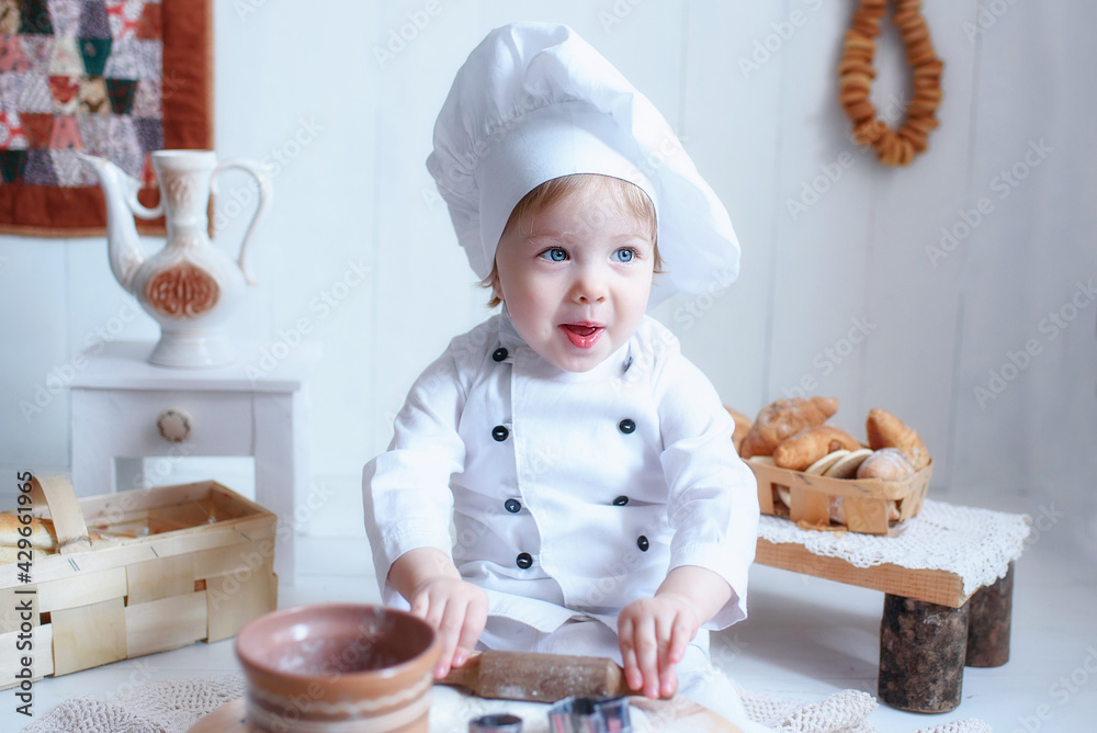 a little girl, blonde, in a white chef's hat, smeared in flour, with bagels around his neck, kneads dough in a brown wooden kitchen, prepares bread and pasta and tries everything a little girl, blonde, in a white chef's hat, smeared in flour, with bagels around his neck, kneads dough in a brown wooden kitchen, prepares bread and pasta and tries everything