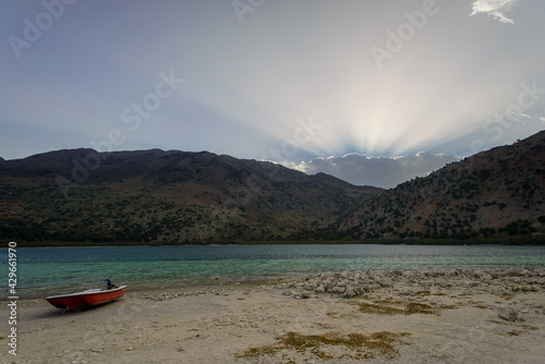 Turquise colour Lake surrounded by moutains  light rays breaking through cloud sunrise © Oskars