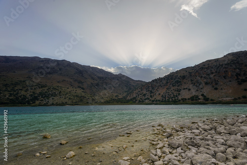 Turquise colour Lake surrounded by moutains  light rays breaking through cloud sunrise © Oskars