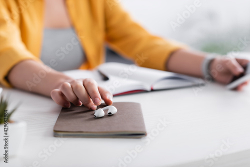 cropped view of woman near wireless earphones and notebook, blurred background