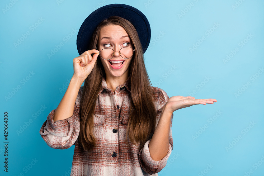 Photo of young happy excited crazy smiling young girl advertising product wear glasses hat isolated on blue color background Photo of young happy excited crazy smiling young girl advertising product wear glasses hat isolated on blue color background