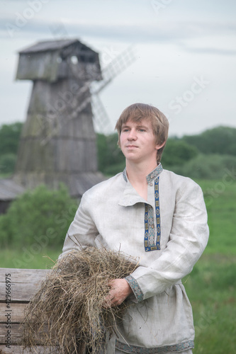 Downshifting concept. A young guy in national clothes lives in an eco-village and earns money from it