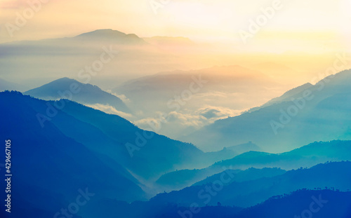 View of Himalayas mountain range with visible silhouettes through the colorful fog at Binsar, a hill station in Almora district, Uttarakhand, India.