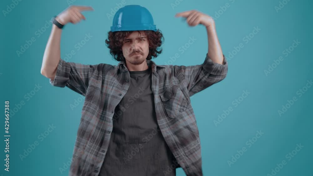 The charismatic young man with the engineer's helmet looks suspiciously at the soup that points to the helmet and displays a like. Isolated on black background, Concept of life. People's emotions. 4k The charismatic young man with the engineer's helmet looks suspiciously at the soup that points to the helmet and displays a like. Isolated on black background, Concept of life. People's emotions. 4k