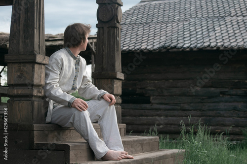 Downshifting concept. A young guy in national clothes lives in an eco-village and earns money from it