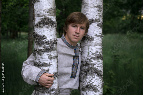 Downshifting concept. A young guy in national clothes lives in an eco-village and earns money from it