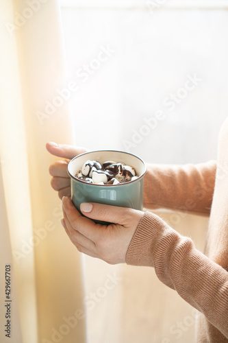 Female hands holding a cup of tasty coffee against the sunny window.