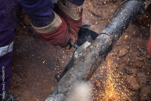 a man in working form is working on production, factory physical labor, a man is holding a Bulgarian, he is sawing an iron pipe with a metal disk, sparks are flying, dangerous work 