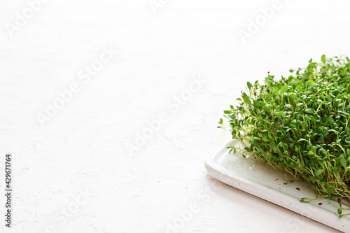 Raw microgreen alfalfa sprouts on a cutting board on a white background.