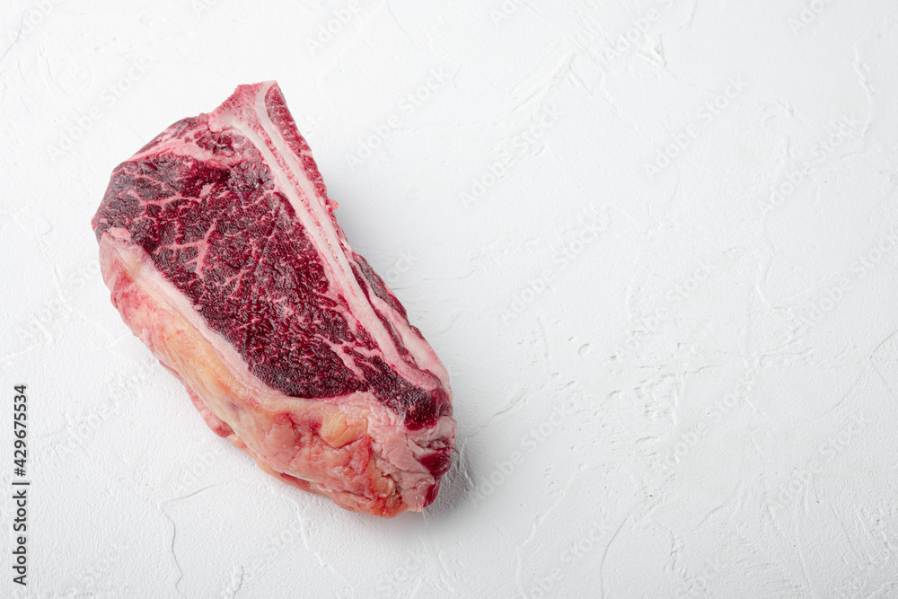 Raw beef meat marbled dry aged Club or striploin on the bone steak, on white stone  background, with copy space for text