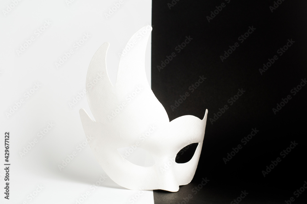 White carnival mask on a black and white background. The mask stands in the middle, between black and white. - obrazy, fototapety, plakaty 