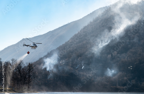 Fire of the Mondonico Mountain above Lake Ghirla with a helicopter that loading water for extinguishing, Valganna, Lombardy, Italy.