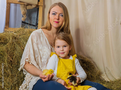 Beautiful, joyful mother with her little daughter are playing with yellow ducklings