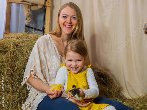 Beautiful, joyful mother with her little daughter are playing with yellow ducklings