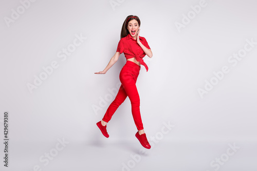 Full length photo of girl jump go palm cheek crazy face wear red dotted blouse pants shoes isolated grey color background