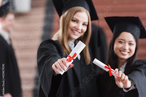 Diplomas in hands of interracial students on blurred background