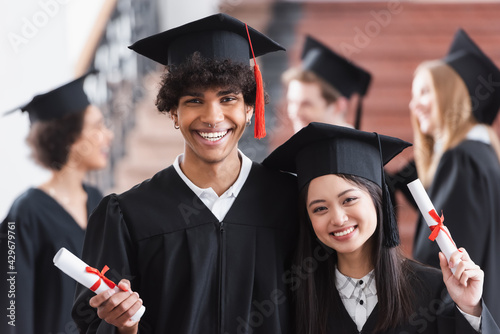 African american bachelor with diploma smiling near asian friend