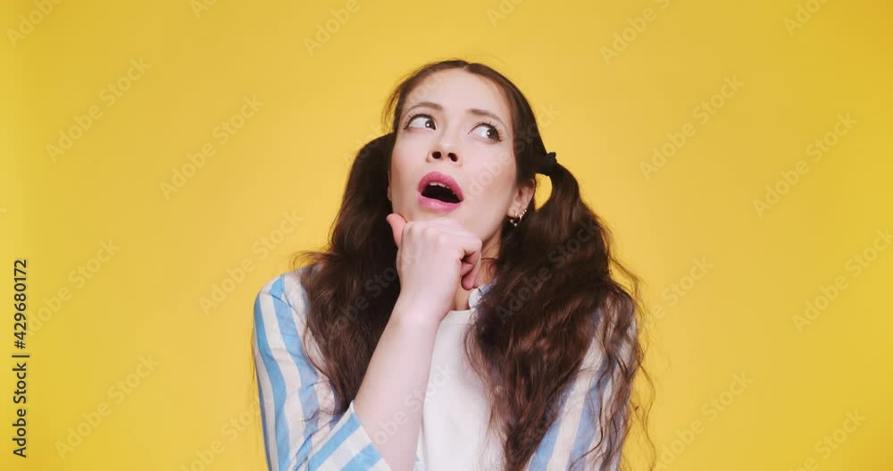 A young beautiful brunette woman with long braids thought about choosing between two different things isolated on yellow background. Concept dilemma of choice and doubts. Copy space what to buy A young beautiful brunette woman with long braids thought about choosing between two different things isolated on yellow background. Concept dilemma of choice and doubts. Copy space what to buy