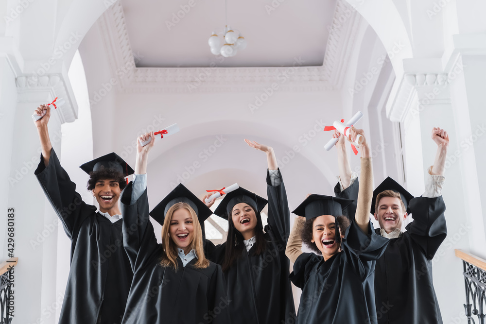 Excited multicultural students with diplomas showing yes gesture