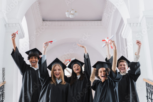 Excited multicultural students with diplomas showing yes gesture