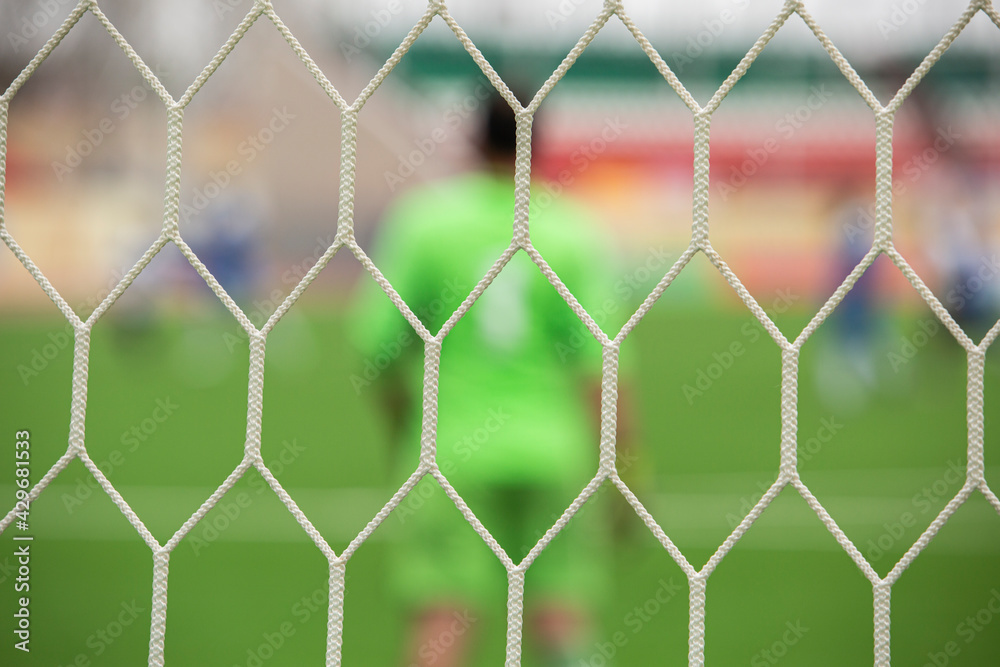 out of focus goalkeeper stands behind the football net in the stadium out of focus goalkeeper stands behind the football net in the stadium