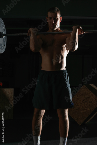 Cuadro en lienzo Close up silhouette of a bodybuilder doing barbel overhead shoulder press in a gym while flexing his muscles portrait