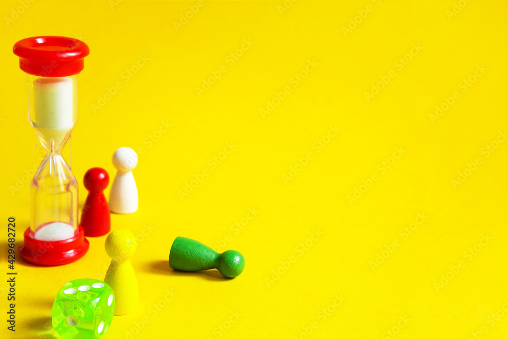 Layout of board games on a yellow background: dice, chips, hourglass timer. Entertainment at home for children and adults. Copy space