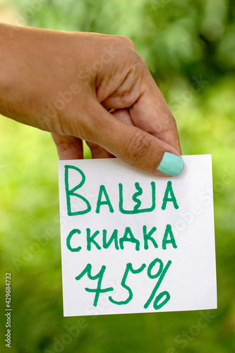 Text Your 75% discount in Cyrillic written on a piece of paper in the hands of a woman