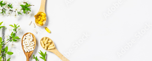 Set of medical capsules with probiotics, omega oils and multivitamins in the wooden spoons with blooming cherry branches on white background. Immunity support supplements. Health care concept.