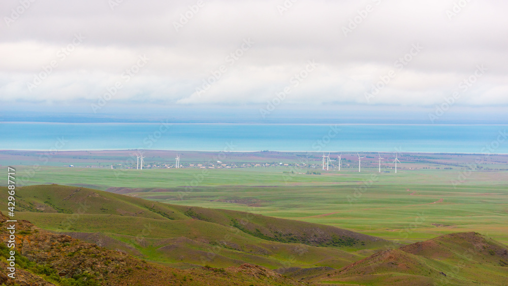Kaphagai lake flat green shores on a overcast day, horizontal stripes of land water and clouds with wind turbines landscape