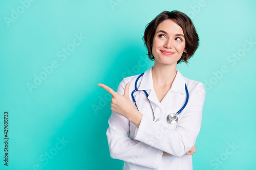 Photo of young woman nurse happy smile look indicate finger empty space ad promo advise choice isolated over teal color background photo