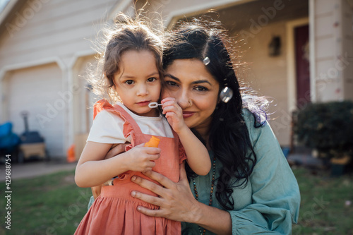 Mom hugging daughter blowing bubbles in front yard
