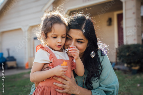 Mom hugging daughter blowing bubbles in front yard