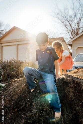Brother and sister playing in pile of dirt in front of home