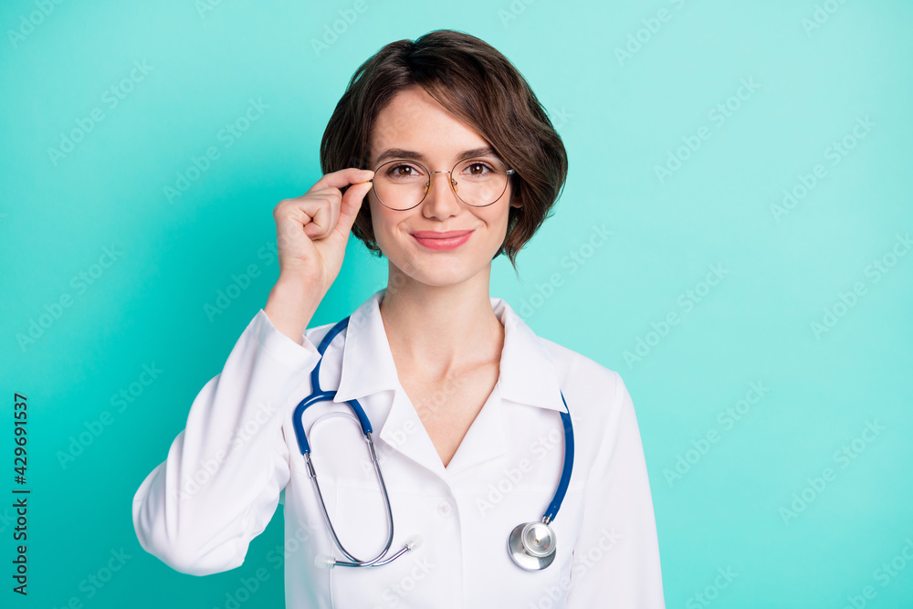 Photo portrait of smiling female doctor wearing white coat isolated on bright teal color background Photo portrait of smiling female doctor wearing white coat isolated on bright teal color background