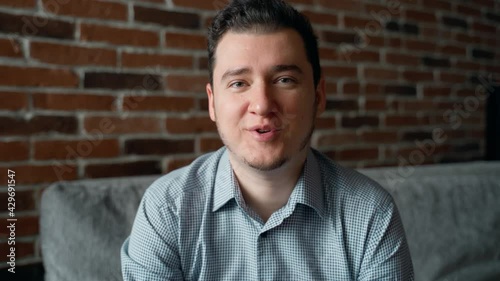 Happy attractive young adult man talking and looking at camera. Video call conference at home concept. Close up headshot greeting man waving hand and smiling