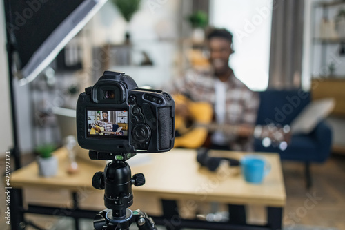 Afro american music teacher recording online tutorial about playing guitar while staying at home. Focus on screen of modern video camera. Concept of people and technology.