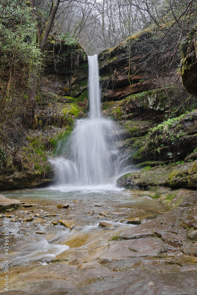 Obraz premium Powerful water of a waterfall splashing down the wet, vivid green moss covered rocks of a cliff during early spring
